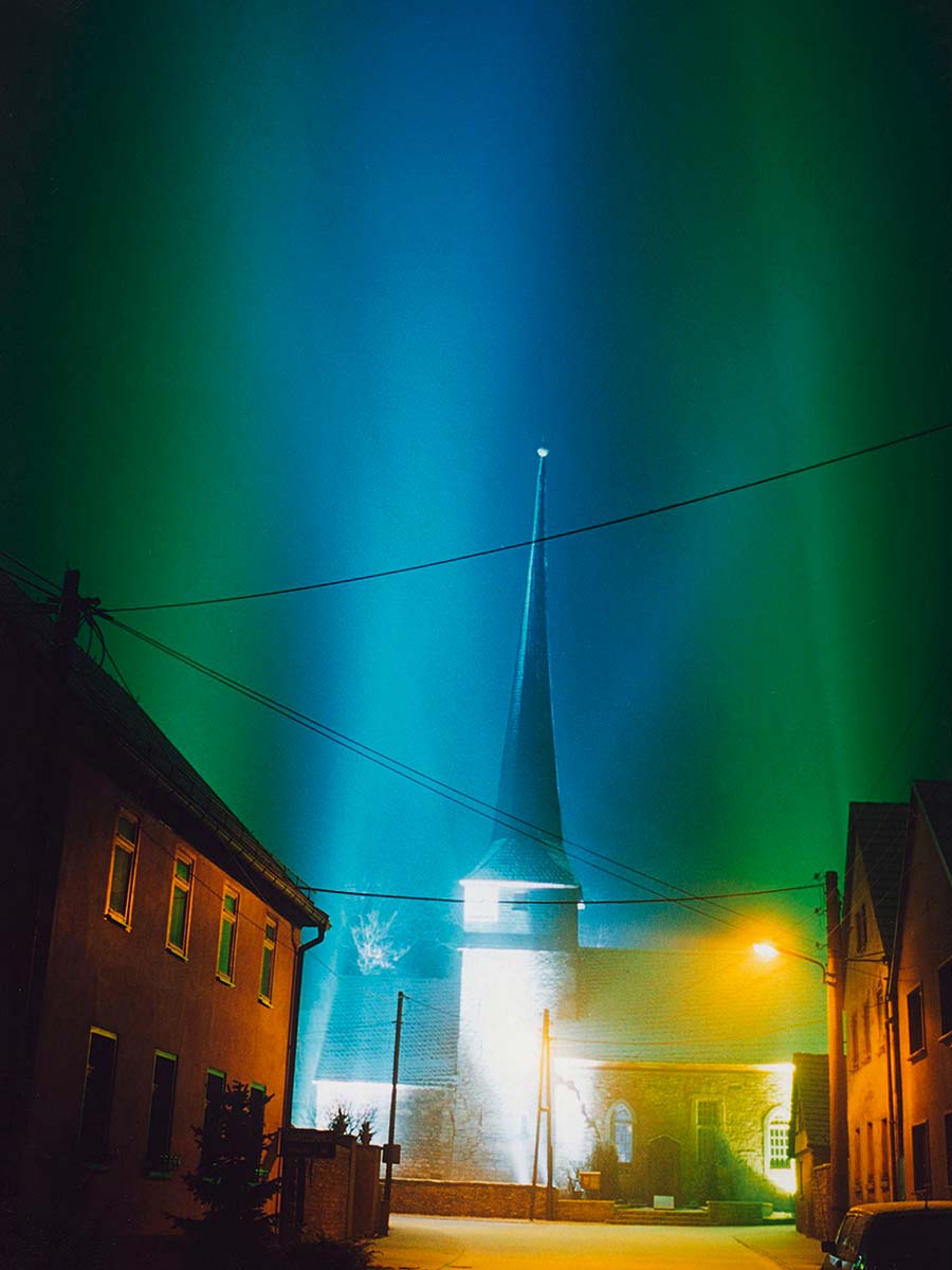 „Lichtskulptur Gelmeroda“ von Peter Mittmann im Jahr 2000. Das farbige Licht von 28 Scheinwerfern verwandelte die Kirche in Weimar-Gelmeroda in eine weithin sichtbare und imposante Wegmarke in Richtung Weimar. Zugleich erinnert ihre strenge Struktur an die berühmten Gemälde des Bauhauskünstlers Lyonel Feininger (1871 – 1956).